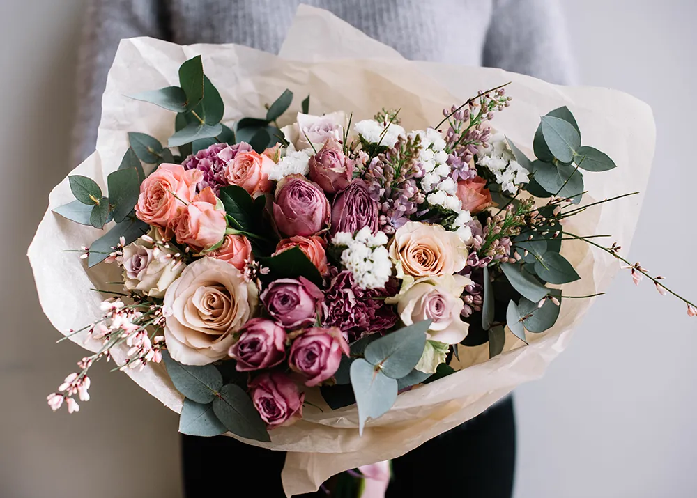 Junge Floristin Frau hält frisch gemacht blühenden Blumenstrauß von Rosen und Eukalyptus auf der grauen Wand Hintergrund.