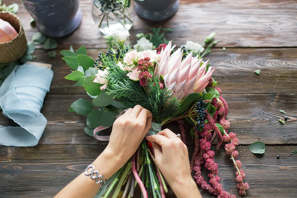 Floristin bei der Arbeit: hübsche junge blonde Frau macht Mode modernen Strauß von verschiedenen Blumen